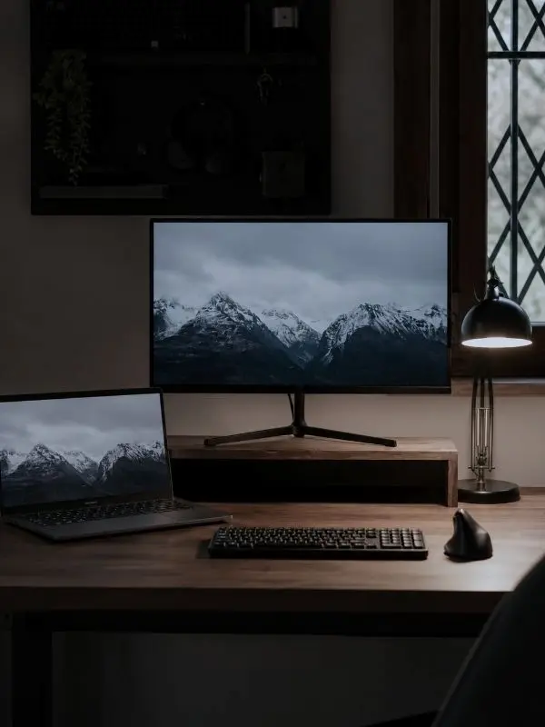 Setup di lavoro con due schermi, mouse e tastiera e una lampada da scrivania accesa